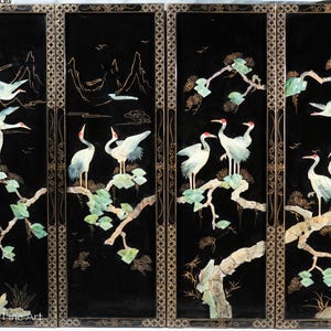 May include: A four-panel black lacquer screen featuring inlaid mother-of-pearl cranes, branches, and foliage. The cranes have red accents and are depicted in flight and perched. The panels are framed with a gold filigree design, creating an elegant Asian-inspired artwork.