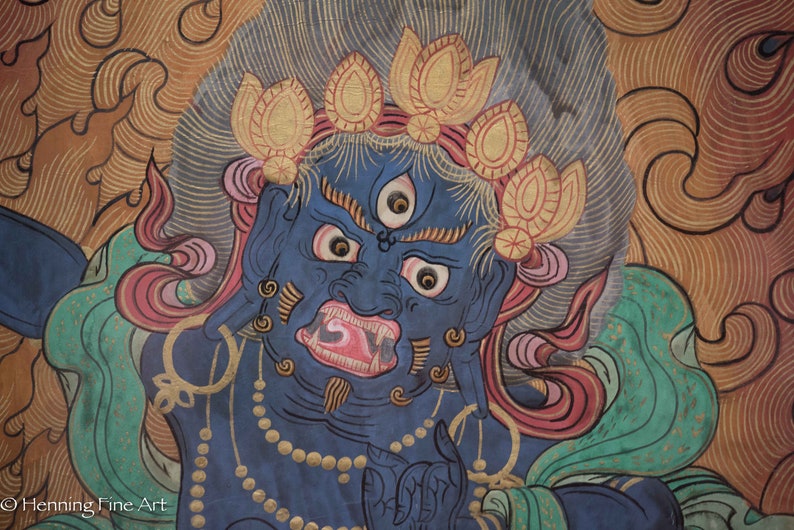May include: A blue deity with a fierce expression, three eyes, and a large mouth with sharp teeth. The deity is adorned with a crown of golden lotus flowers and a necklace of pearls. The background is a swirling pattern of gold and red.
