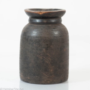 May include: A dark brown, handcrafted wooden jar with a wide, flared top and a cylindrical body. The jar features horizontal etched lines around the body and a slightly lighter brown rim. The jar is likely used for storage or decorative purposes.