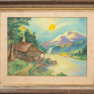 May include: A framed pastel painting depicts a rustic log cabin nestled beside a lake, with a mountain range in the background. The artwork features a bright yellow sun, a waterfall, and lush green trees, creating a serene landscape scene.