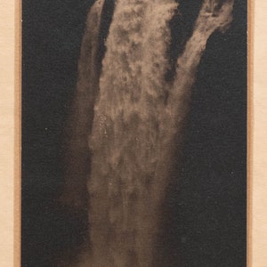 May include: A black and white photograph of a waterfall cascading down a rocky cliff. The waterfall is surrounded by a dark forest, and the sky is a light gray. The image is framed in a brown border.