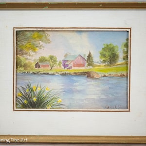 May include: A watercolor painting of a rural landscape with a red barn, a smaller building, and a river in the foreground. The painting is framed in a gold frame and signed "Grace C. Simcox".