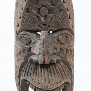 May include: A carved wooden mask with a detailed face. The mask has a wide open mouth, detailed eyes, and intricate carvings. The color is a dark brown. The mask is likely a decorative or ceremonial item.
