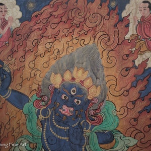 May include: A blue deity with three eyes and a fierce expression, surrounded by flames, is depicted in this traditional Tibetan painting. The deity is adorned with a crown of golden lotus flowers and a necklace of pearls. The painting is set against a background of swirling clouds and a blue sky.