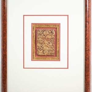 May include: A framed gold and red artwork with a textured, abstract design. The artwork is framed in a dark wood frame.