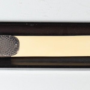 May include: A vintage letter opener with a silver hammered metal handle and a cream-colored blade, resting in a black rectangular tray. The opener is a classic desk accessory.