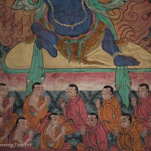 May include: A colorful painting depicting a deity surrounded by figures in prayer. The deity is blue with a gold crown and sits on a throne. The figures are dressed in red, orange, and yellow robes and have their hands clasped in prayer.