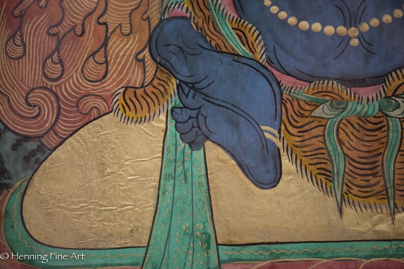 May include: A close-up of a colorful painting depicting a deity with a blue foot and a gold background. The deity is wearing a blue robe with a gold trim and a green sash. The painting is on a canvas and has a textured surface.