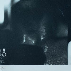 May include: Monochrome poster showing a man in sunglasses. The USA Olympic rings logo is in the lower left corner. The poster is a promotional item for the 1992 US Olympic Team.