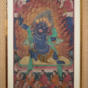 May include: A colorful Tibetan Buddhist painting depicting a deity with multiple eyes and a fierce expression, surrounded by flames and seated on a throne.  The deity is surrounded by a group of figures in prayer.