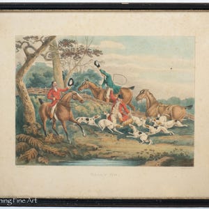 May include: An antique framed print depicting a fox hunt scene. The artwork features riders on horseback, hounds, and a natural landscape with trees and a stream. The print is in a black frame.