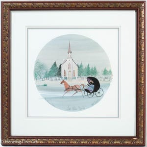 May include: Framed artwork featuring a watercolor painting of a white church with a steeple, a horse-drawn carriage, and evergreen trees. The artwork is set within a circular scene, framed by a brown wooden frame with decorative edges. The text "Little White Church" is visible.