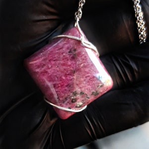 May include: A pink gemstone pendant with silver wire wrapping. The pendant is hanging from a silver chain.
