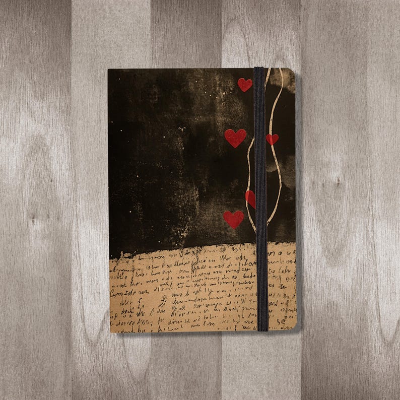 May include: A black journal with a black elastic band closure. The cover has a distressed look with red hearts and handwritten text.