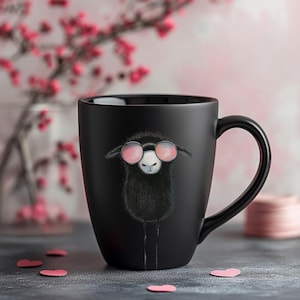 May include: Black ceramic mug with a white sheep wearing pink sunglasses. The mug has a black handle.