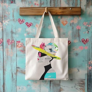 May include: White canvas tote bag with a colorful graphic of a woman wearing a large hat and sunglasses. The hat is made of yellow, blue, and pink paper with a newspaper print design. The woman's face is partially obscured by the hat.