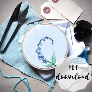 May include: A close-up of a blue and green floral embroidery design in a wooden embroidery hoop. The hoop is on a white fabric with a blue fabric underneath. The text "PDF download" is in the lower right corner of the image.