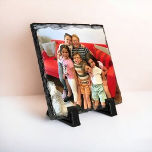 May include: A family portrait printed on a slate photo frame. The photo shows a group of five people, including a grandmother and four grandchildren, smiling and posing together. The frame is made of natural slate and has a rustic look.