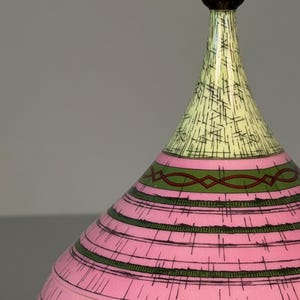 May include: A decorative lidded vessel with a rounded dark brown base, a wide midsection featuring horizontal pink bands with dark green cross-hatching, and a tapered light yellow top section with a dark brown spherical finial at the peak.