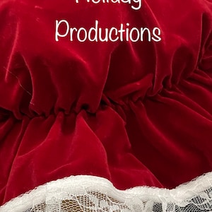 Pu&ograve; includere: Primo piano di un cappello di velluto rosso con finiture in pizzo bianco. Il testo "Holiday Productions" &egrave; scritto in bianco sulla parte superiore del cappello. Il cappello ha un design a balze.