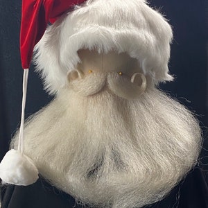 May include: A Santa Claus costume headpiece featuring a red velvet hat, a white faux fur wig, and a long, white beard. The beard and wig are made of a soft, fluffy material. The hat has a white pom-pom attached by a white string.