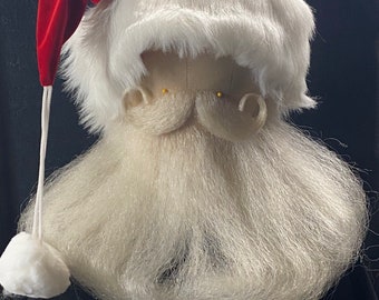 May include: A Santa Claus costume headpiece featuring a red velvet hat, a white faux fur wig, and a long, white beard. The beard and wig are made of a soft, fluffy material. The hat has a white pom-pom attached by a white string.