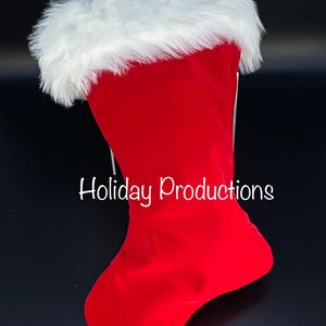 May include: Red velvet Christmas stocking with a white faux fur cuff. The stocking is hanging from a hook and the text "Holiday Productions" is visible on the stocking.