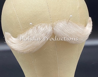May include: A light beige mannequin head with a pair of light blonde mustaches pinned to it. The text "Holiday Productions" is visible at the top of the image. The mustaches are curved and fluffy.