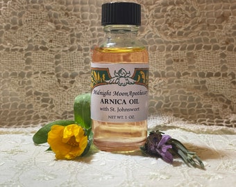 Op de afbeelding: Een klein glazen flesje met een zwarte dop, gevuld met een lichtgele vloeistof. Het etiket vermeldt "Midnight Moon Apothecary Arnica Oil with St. Johnswort NET WT. 1 OZ."