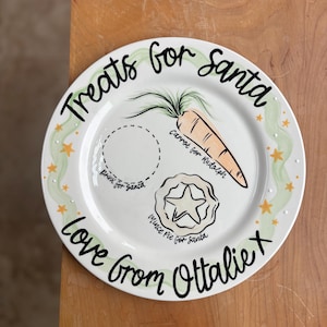 May include: A white ceramic plate with a festive design. The plate features the text "Treats for Santa" and "Love From Ottalie X". It includes illustrations of a carrot, a mince pie, and areas for drinks and treats.