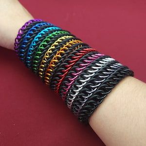 May include: A stack of colorful metal bracelets in a rainbow pattern, with a black metal bracelet at the bottom.