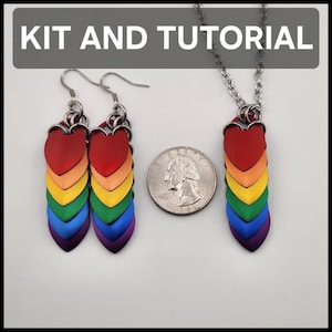 May include: A set of rainbow-colored jewelry, including earrings and a necklace, with a heart-shaped top and a scale-like design. The text "KIT AND TUTORIAL" is displayed above the jewelry. A quarter is next to the jewelry.