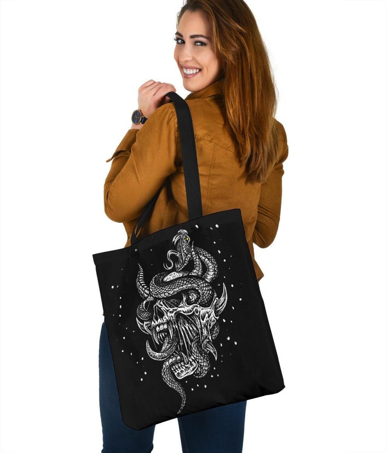 Op de afbeelding: Zwarte tote bag met een witte afbeelding van een schedel met een slang eromheen gewikkeld. De slang heeft een geel oog.
