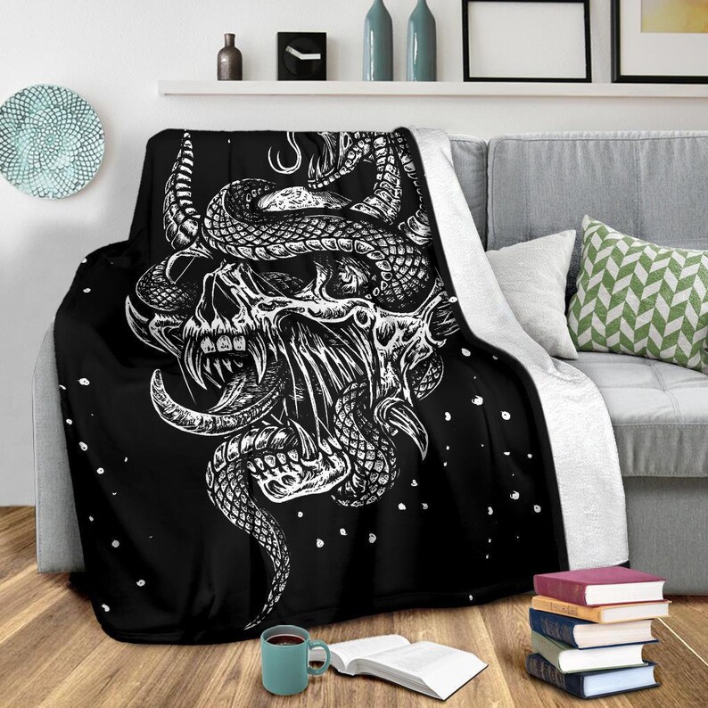 May include: Black and white throw blanket with a graphic design of a skull with a snake wrapped around it. The background is black with white dots.