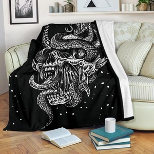 May include: Black and white throw blanket with a graphic design of a skull with a snake wrapped around it. The design is on a black background with white dots.