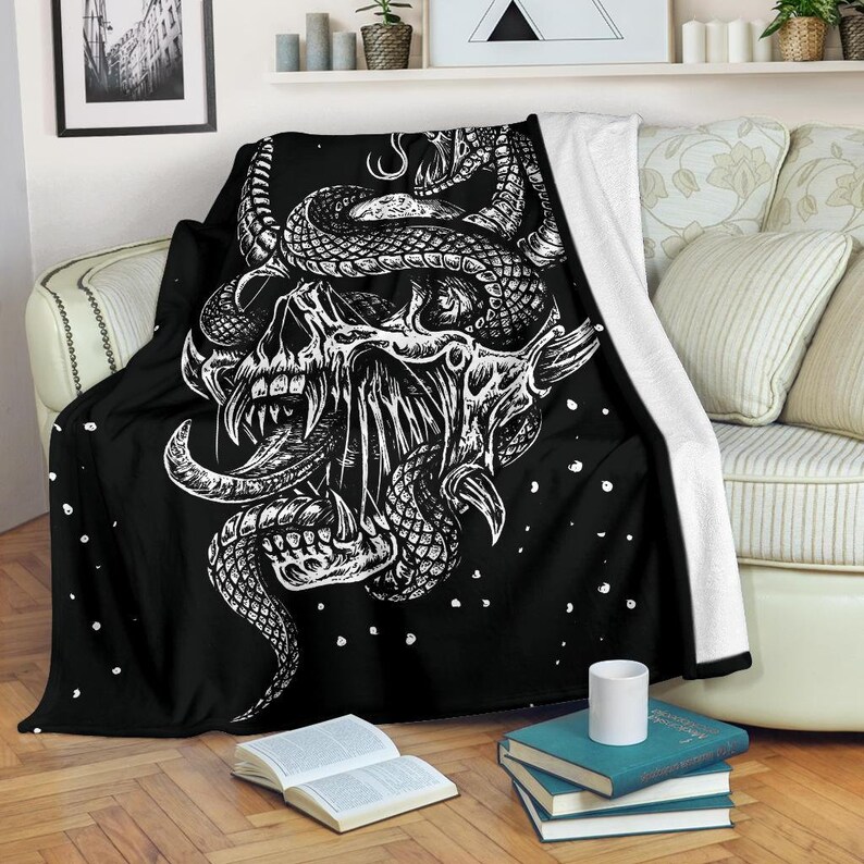 May include: Black and white throw blanket with a graphic design of a skull with a snake wrapped around it. The design is on a black background with white dots.