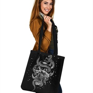 Op de afbeelding: Zwarte tote bag met een witte afbeelding van een schedel met een slang eromheen gewikkeld. De slang heeft een geel oog.