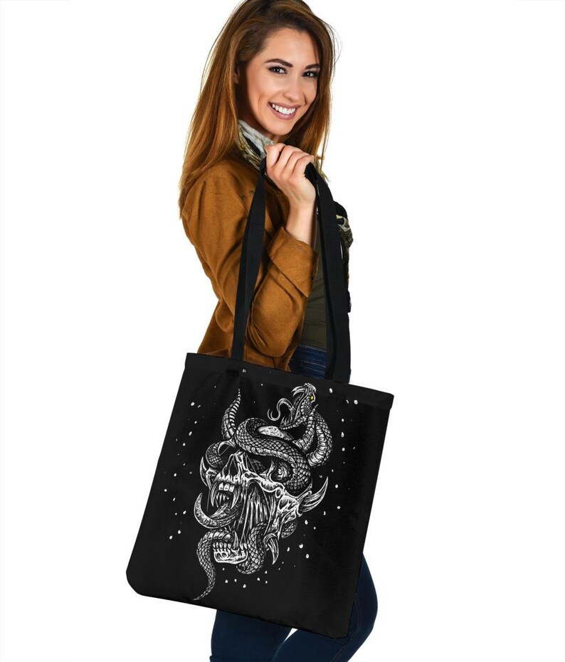 Op de afbeelding: Zwarte tote bag met een witte afbeelding van een schedel met een slang eromheen gewikkeld. De slang heeft een geel oog.