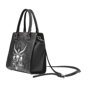 May include: Black leather handbag with a white graphic of an angel with wings and a cross. The bag has a top handle and a detachable shoulder strap.