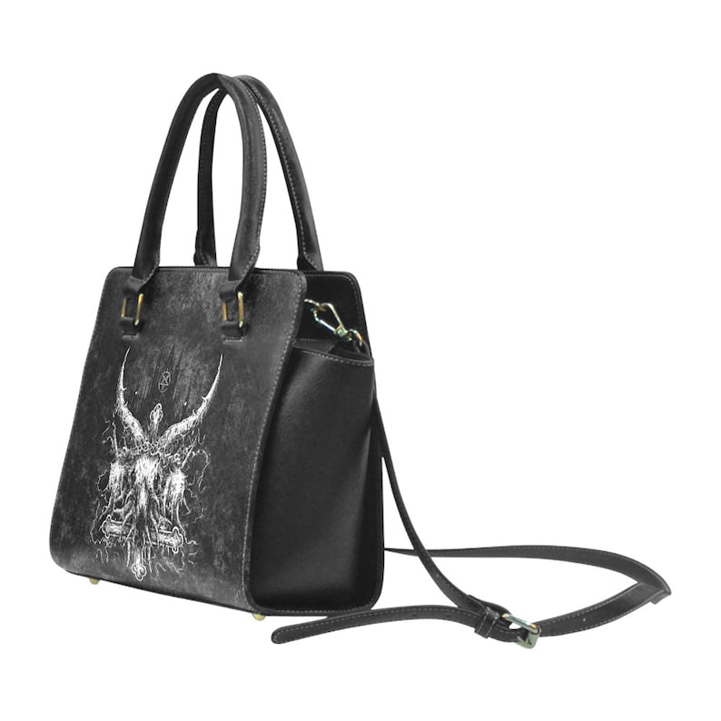 May include: Black leather handbag with a white graphic of an angel with wings and a cross. The bag has a top handle and a detachable shoulder strap.