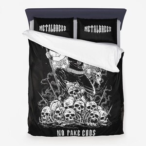 Könnte beinhalten: Schwarzer und weißer Bettbezug mit einem grafischen Druck einer Person, die auf einem Schädelhaufen steht. Der Text "NO FAKE GODS" ist unten auf dem Bettbezug aufgedruckt. Die Kissenbezüge haben den Text "METALBRED" aufgedruckt.