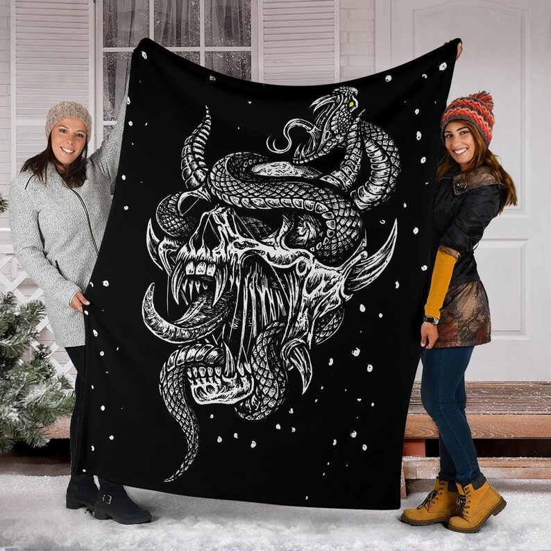 May include: Black and white fleece blanket with a graphic design of a skull with a snake wrapped around it. The skull has sharp teeth and a long tongue. The snake has a detailed pattern.