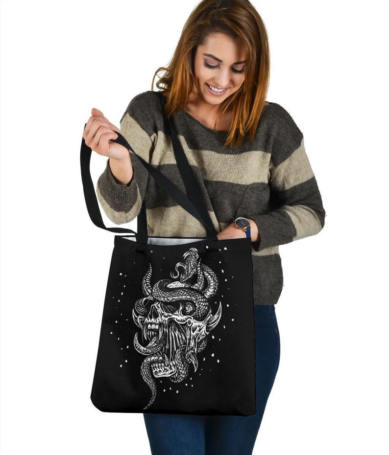 Op de afbeelding: Zwarte tote bag met een witte afbeelding van een schedel met een slang eromheen gewikkeld. De slang heeft een wit oog en de schedel heeft een witte mond met tanden.