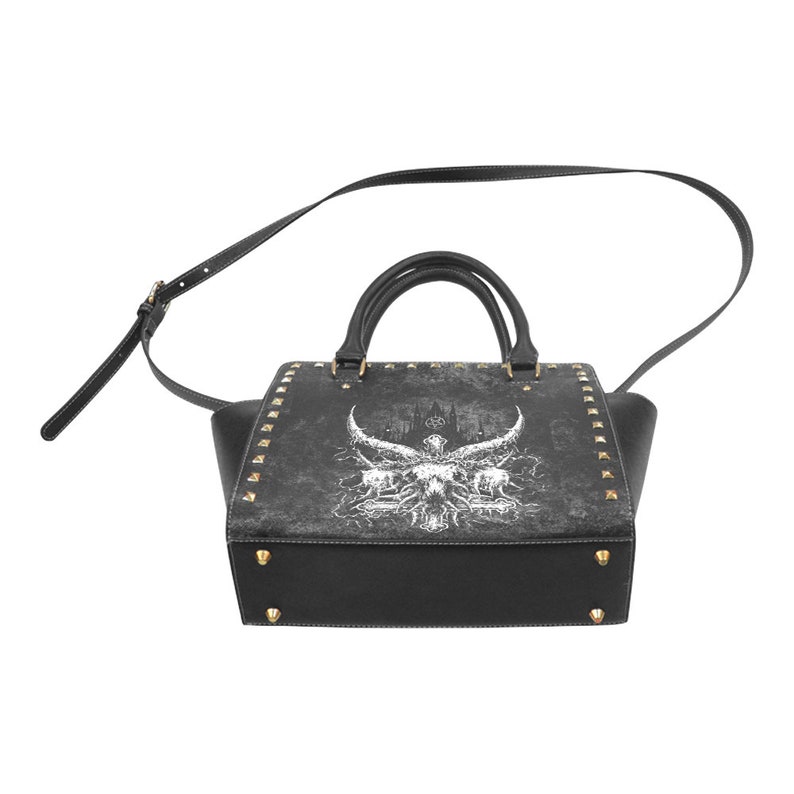 May include: Black leather handbag with a gold-tone studded design. The bag features a white graphic print of a skull with horns and a gothic castle in the background.
