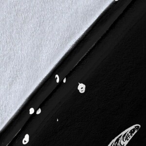 May include: A black fabric with a white pattern of small circles and a larger, abstract shape. The fabric is folded in half, with the white side facing up.