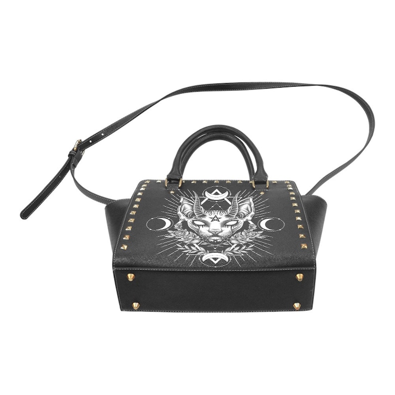 Op de afbeelding: Zwarte leren handtas met een witte afbeelding van een kat met hoorns en een pentagram. De tas heeft gouden studs en een schouderband.