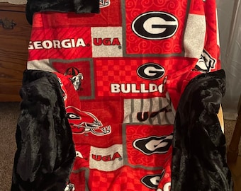 May include: Red and black fleece blanket with a patchwork design featuring the University of Georgia Bulldogs logo, the letters UGA, and the words "Bulldogs" and "Georgia".