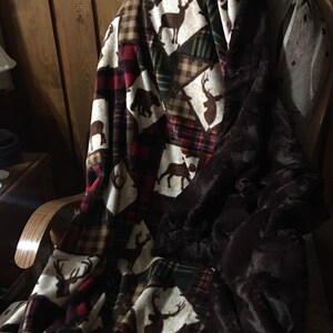 May include: A brown and white plaid throw blanket with a brown faux fur trim. The blanket is folded and draped over a wooden rocking chair. The blanket features a repeating pattern of deer, bears, and plaid.