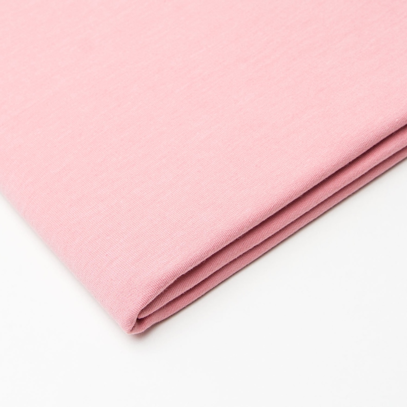 Puede incluir: Un trozo de tela suave y rosa doblado. La tela tiene una textura suave y un brillo sutil.