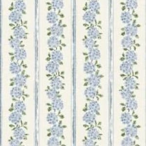 Op de afbeelding: Een stofpatroon met verticale strepen van lichtblauwe hortensiabloemtrossen die afwisselen met dunne, verweerde blauwe krijtstrepen op een effen gebroken witte achtergrond. Het bloemmotief herhaalt zich in een doorlopende verticale opstelling.